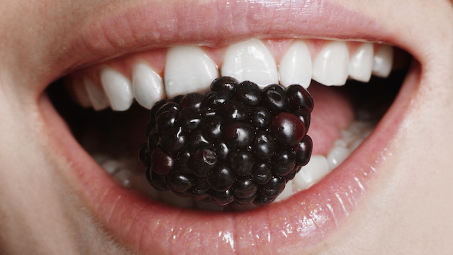 Young woman holding blackberry in teeth, close-up of mouth