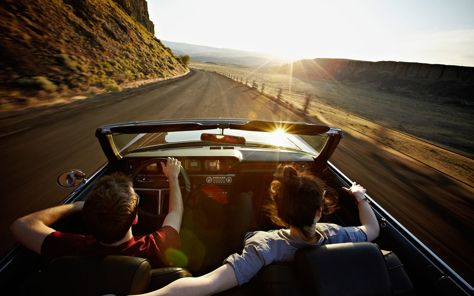 Young couple driving convertible at sunset on desert road